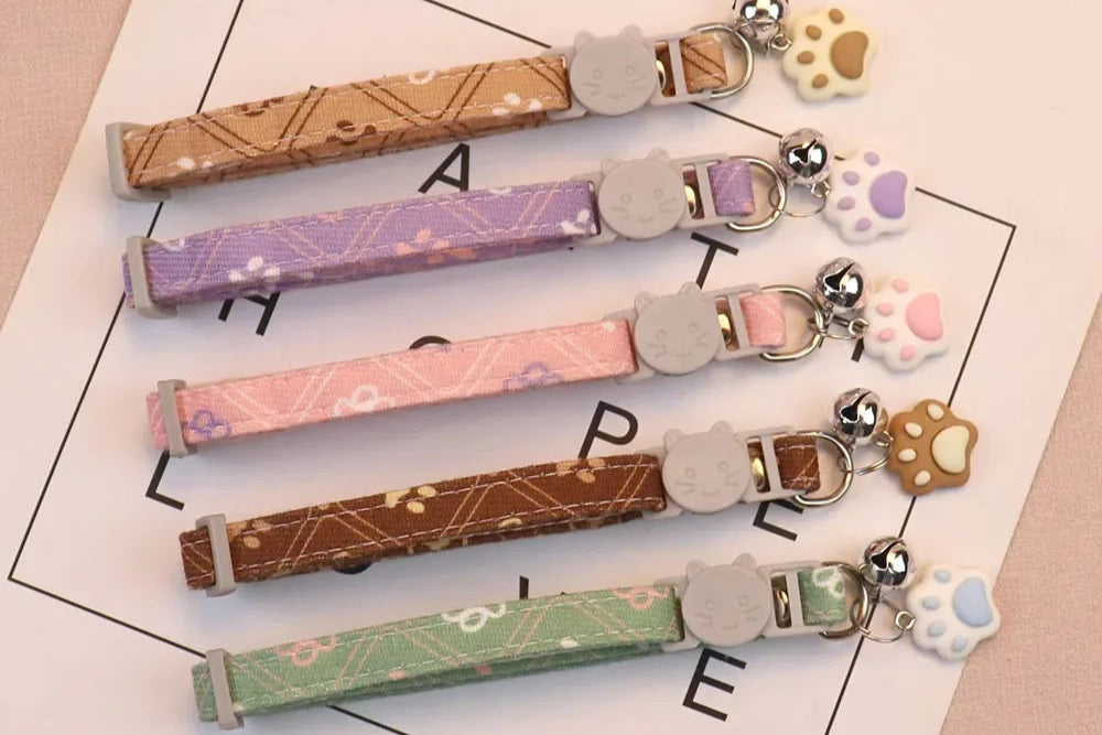 Collier en tissu pour chat avec un motif d'empreintes de pattes et une clochette argentée.